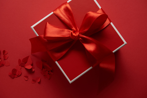 top view of red present with silk ribbon and paper cut hearts on red background - Foto, Imagem