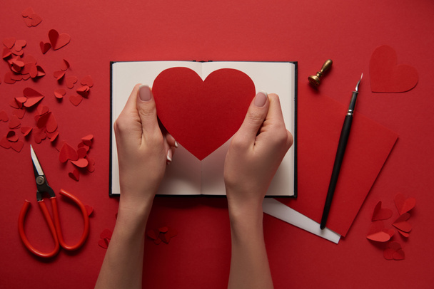 cropped view of woman holding blank paper cut heart sign on red background - 写真・画像