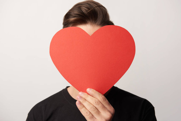 hombre con cara oscura sosteniendo papel vacío tarjeta de corazón cortado aislado en gris
 - Foto, imagen