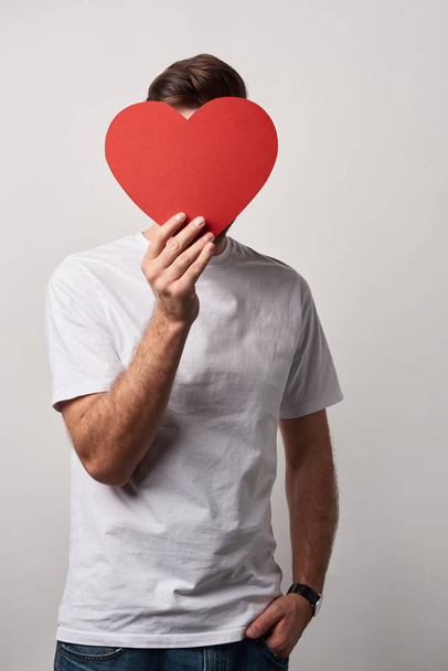 man with obscure face and hand in pocket holding empty paper cut heart card  - Fotoğraf, Görsel