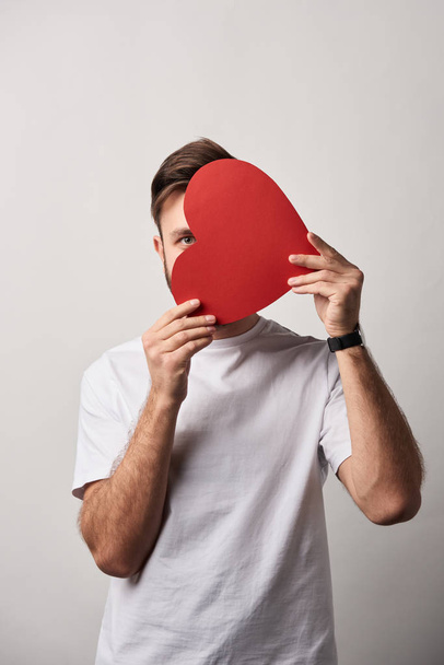 man hiding face behind blank paper cut heart card on grey background - Photo, Image