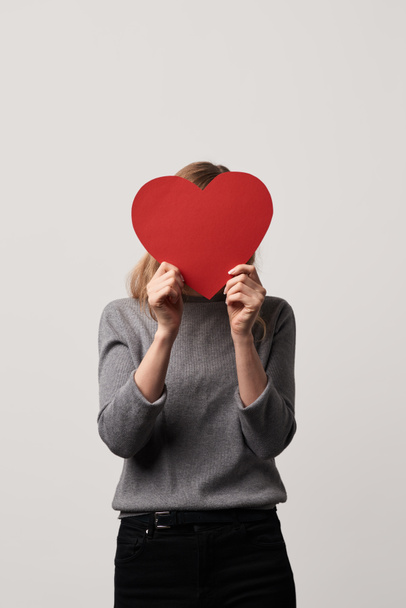 jeune femme cachant visage derrière papier rouge vide carte de coeur coupé isolé sur gris
  - Photo, image