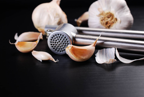 fresh garlic bulbs and cloves with presser lying on black background with copy space for own text  - Foto, afbeelding