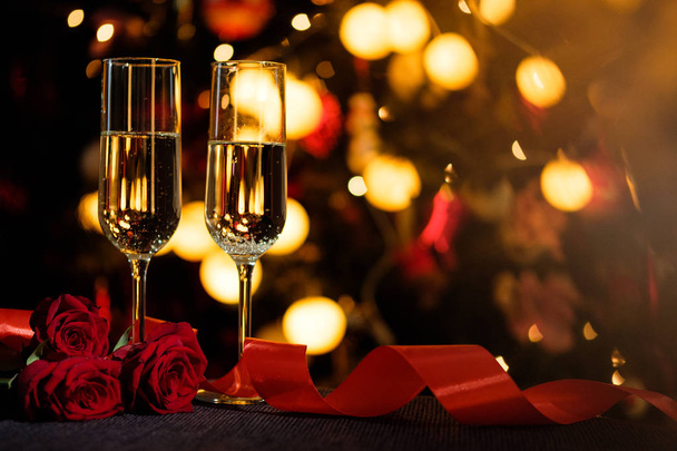 Glasses of champagne on the background of lights with roses and red ribbon - Photo, image