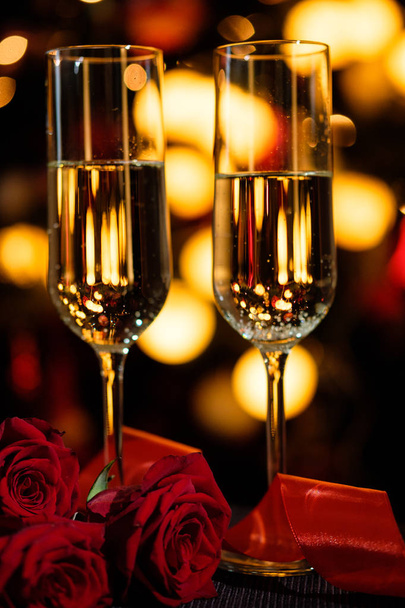 Glasses of champagne on the background of lights with roses and red ribbon - Foto, Imagen