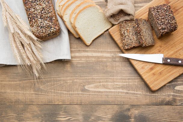 Cut with slices and whole grain and white bread on a wooden board. A loaf of fresh rustic whole meal rye bread, sliced on a wooden board, rural food background. Top view. - 写真・画像