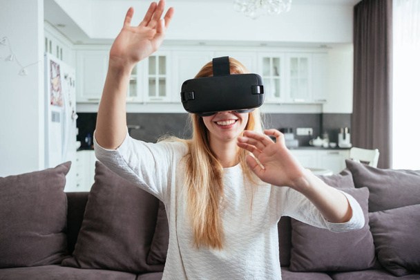 Молода блондинка вдома з сучасним дизайном ставить окуляри віртуальної реальності
 - Фото, зображення