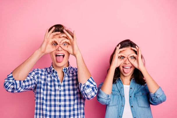Close up portrait of two she her he him his boy lady showing v-sign near eyes in shape figure of specs joking tongue out wearing casual shirts denim plaid outfit isolated on rose background - Foto, Bild