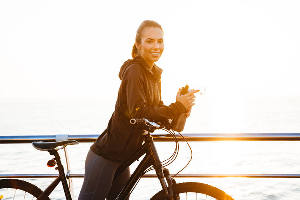 Photo of european woman riding bicycle on boardwalk during sunrise over sea - Φωτογραφία, εικόνα
