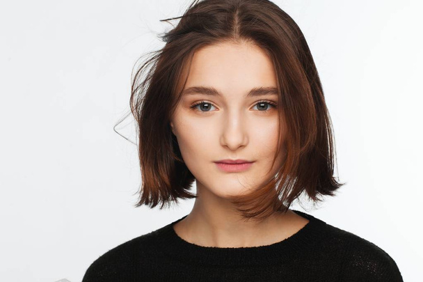 Portrait of a beautiful teen girl in a black sweater on a white background. Fan-blown hair - Zdjęcie, obraz