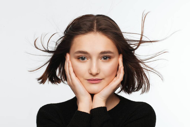 Portrait of a beautiful teen girl in a black sweater on a white background. Fan-blown hair - 写真・画像