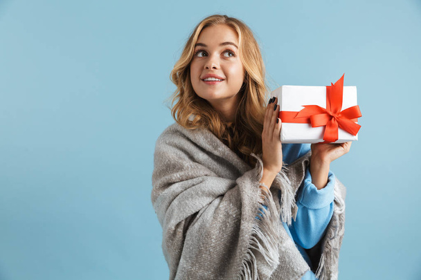 Image of joyful woman 20s wrapped in blanket holding present box isolated over blue background - Φωτογραφία, εικόνα