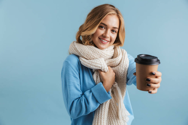 Image of charming woman 20s wrapped in scarf smiling and holding takeaway coffee isolated over blue background - Foto, imagen