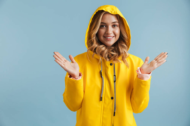 Image of joyful woman 20s wearing yellow raincoat looking at camera isolated over blue background - Foto, Imagen