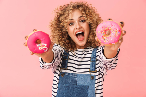 Photo of glamour curly woman 20s wearing casual clothes holding donuts while standing isolated over pink background - Valokuva, kuva