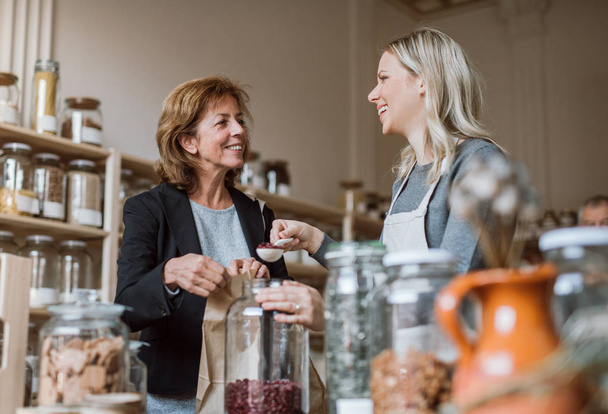 A female shop assistant serving a senior customer in a zero-waste shop. - Photo, Image