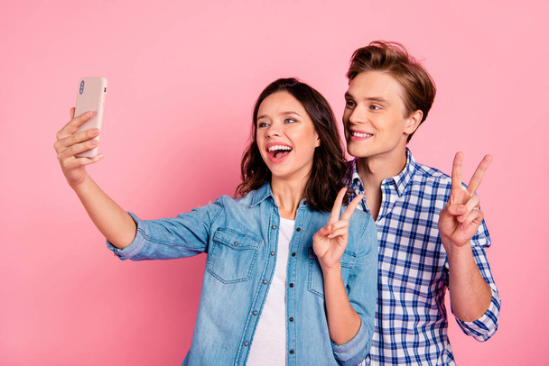 Portrait of nice lovely attractive cheerful positive couple holding in hands device gadget taking making selfie showing v-sign isolated over pink pastel background - Fotó, kép