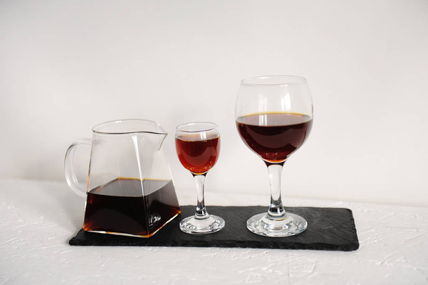 試飲のための 2 つのワイングラスの透明なサービング ティーポットにコーヒー。白い背景の上のスレート ボードで提供しています. - 写真・画像