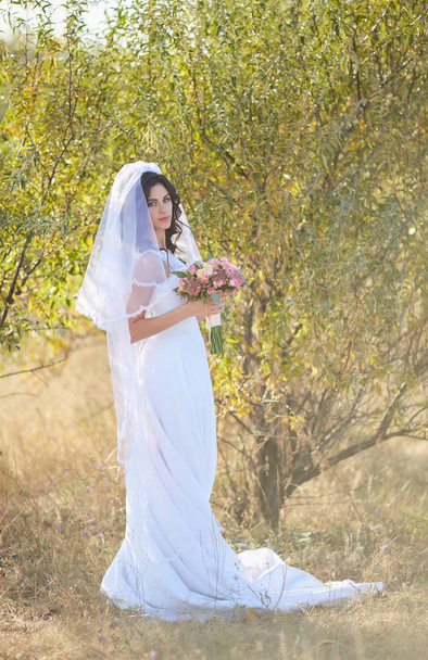 Красивая улыбающаяся невеста в натуральном цветочном венке и стоит на золотых летних полях с эвкалиптом в руках
. - Фото, изображение