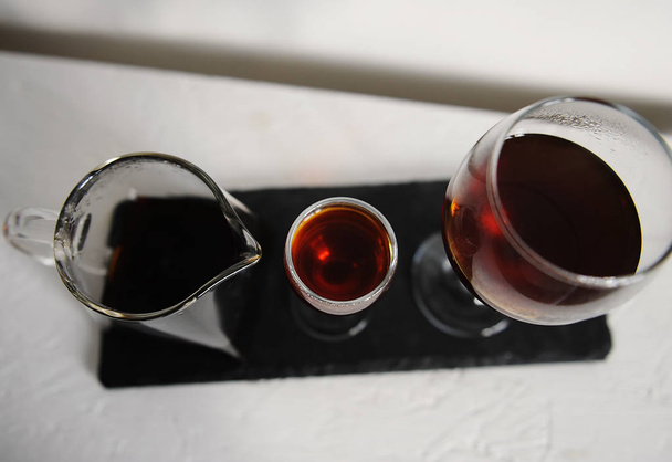 Café em um bule de chá de serviço transparente de dois copos de vinho para degustação. Servido em uma tábua de ardósia em um fundo branco
. - Foto, Imagem