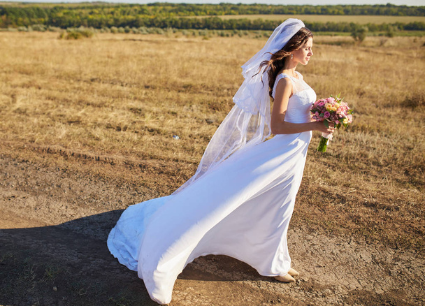 Krásná usměvavá nevěsta na sobě přirozenou květinový věnec a stojí v polích zlaté letní s eukalyptu v rukou. - Fotografie, Obrázek