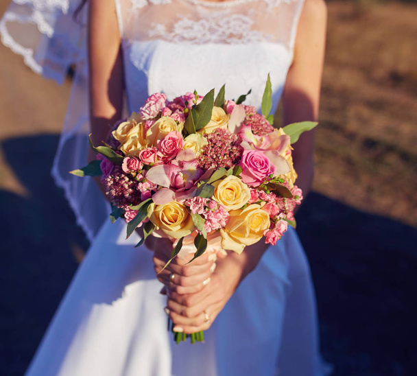 Bella sposa sorridente che indossa una corona di fiori naturali e in piedi nei campi estivi dorati con eucalipto in mano
. - Foto, immagini
