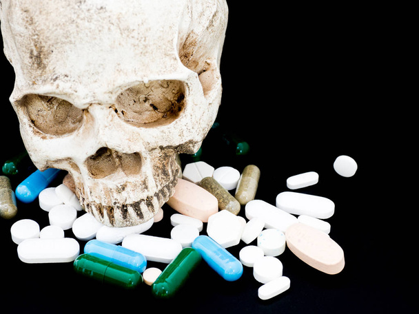 Ludzka czaszka na wielobarwny narkotyków i kapsułka jest na czarnym tle. Z bliska. Jesteśmy przeciwko narkotykom (anti leki), leczyć w kontener dla zdrowia. Kupie zielony niebieski biały okrągły kapsułki pigułki - Zdjęcie, obraz