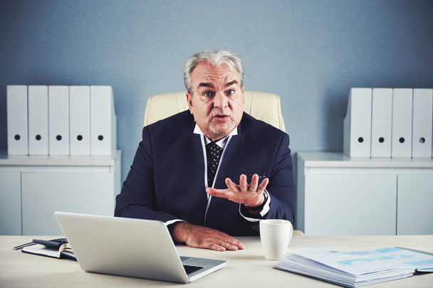 convincing aged business man sitting at office desk table and gesture with hand - Foto, immagini