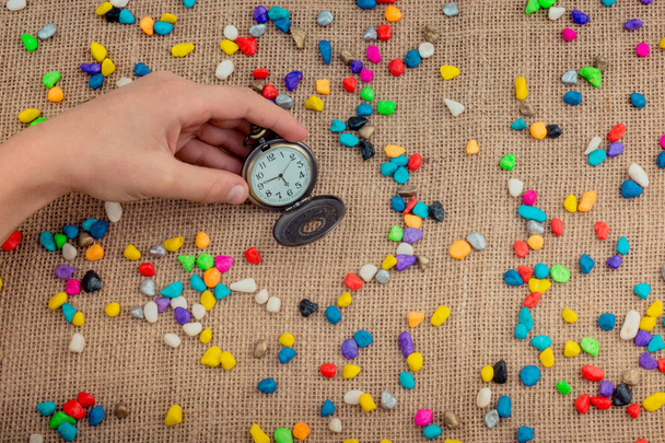 Pocket watch amid colorful pebbles on canvas background - Photo, Image