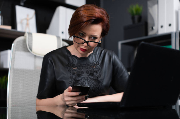 Tyylikäs nainen työskentelee kannettavan tietokoneen ja puhelimen toimistossa
 - Valokuva, kuva