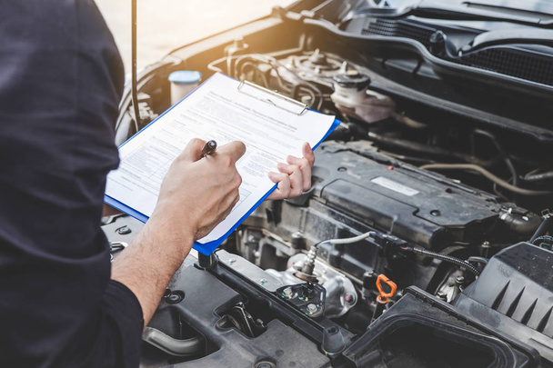 Services car engine machine concept, Automobile mechanic repairman checking a car engine with inspecting writing to the clipboard the checklist for repair machine, car service and maintenance. - Photo, Image