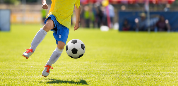 若いサッカー プレーヤーを蹴るボール。背景にぼやけピッチ水平サッカー試合画像 - 写真・画像