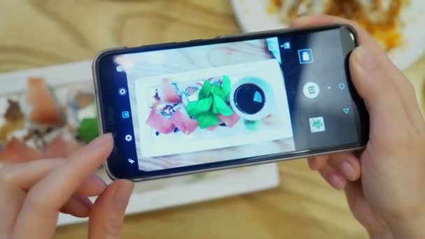 primo piano. Le mani femminili scattano una foto di sushi su uno smartphone in un ristorante
. - Filmati, video