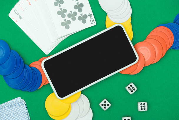κάτοψη του πράσινου πόκερ τραπέζι με πολύχρωμα τσιπ, ζάρια, χαρτιά και smartphone - Φωτογραφία, εικόνα