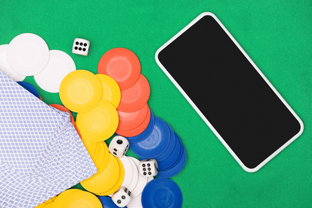 bovenaanzicht van groene pokertafel met veelkleurige chips, speelkaarten, dobbelstenen en smartphone - Foto, afbeelding