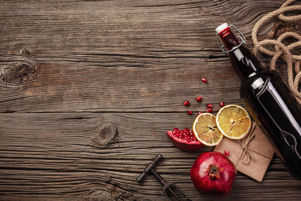 reife Granatapfelfrüchte mit einem Glas Wein, einer Flasche und einem Korkenzieher auf Holzgrund. Ansicht von oben mit Kopierraum. - Foto, Bild
