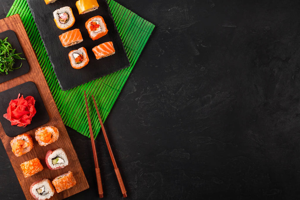 Conjunto de sushi com wasabi e gengibre na bandeja de pedra preta na mesa preta. Vista superior
. - Foto, Imagem