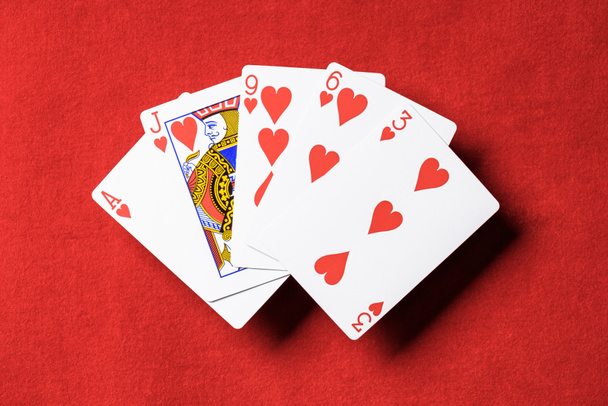 top view of red poker table and unfolded playing cards with hearts suit - Fotografie, Obrázek