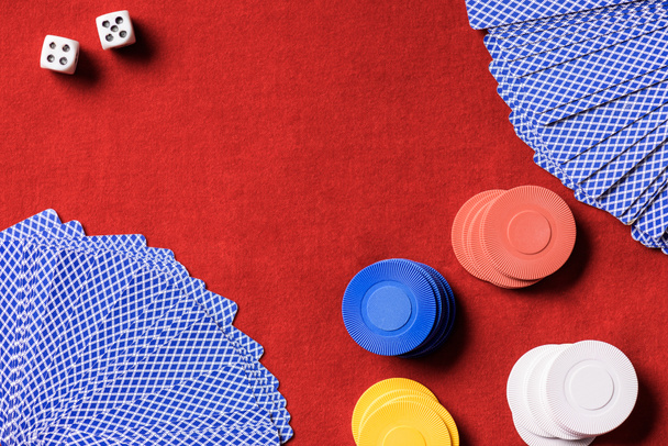 bovenaanzicht van rode pokertafel met veelkleurige chips, dobbelstenen en ongevouwen kaarten - Foto, afbeelding