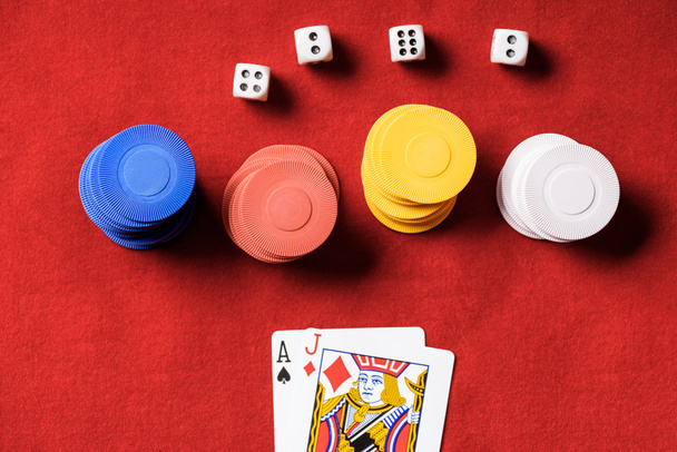 top view of red poker table with multicolored chips, dices and two unfolded cards - Fotoğraf, Görsel