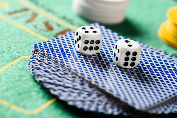 selective focus of dices on playing cards in deck with chips and green poker table on background - Foto, imagen