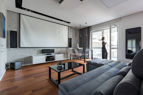 Сіра і біла вітальня з диваном, столом, балконом і екраном проектора
 - Фото, зображення
