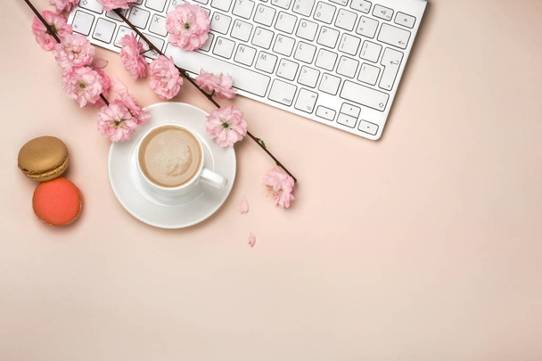 Белая чашка с капучино, цветками сакуры, клавиатура на розовом фоне. Вид сверху
. - Фото, изображение
