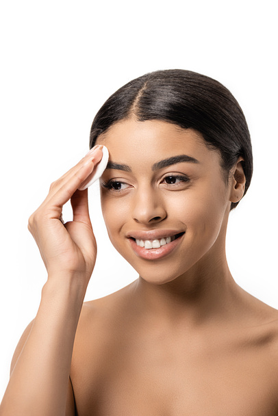 heureuse jeune femme afro-américaine nettoyage visage avec disque de coton isolé sur blanc
 - Photo, image