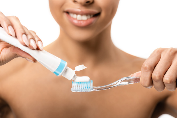 przycięte strzał uśmiechający się młodych african american kobieta trzymając szczoteczkę do zębów i pasty do zębów, na białym tle  - Zdjęcie, obraz