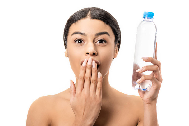 shocked young african american woman holding bottle of water and looking at camera isolated on white - Photo, Image
