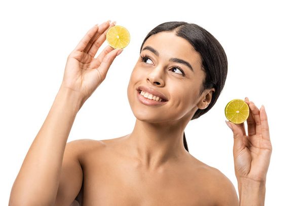 smiling naked african american girl holding halves of lime and looking up isolated on white - Zdjęcie, obraz