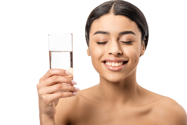 happy young african american woman with closed eyes smiling and holding glass of clear water isolated on white - Foto, immagini