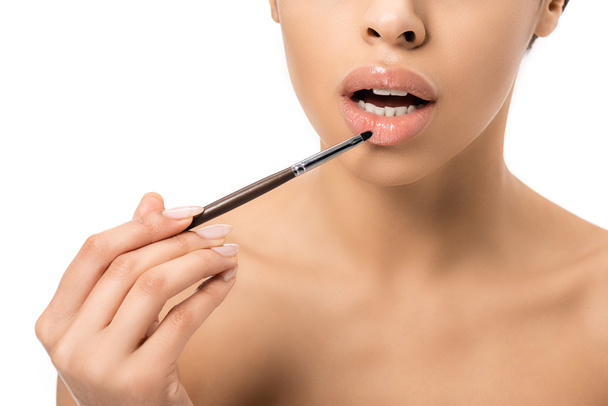 cropped shot of naked young african american woman applying lipstick with cosmetic brush isolated on white - Фото, изображение