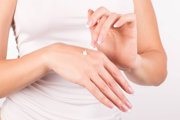 Female hands with french manicure applying hand cream, white background, closeup, front view - Φωτογραφία, εικόνα